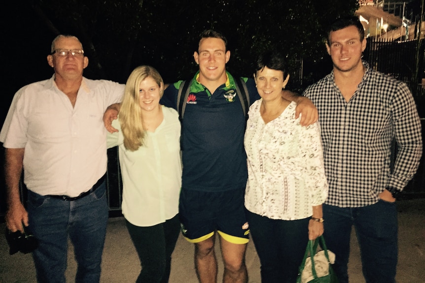 A family of five stand in a row, smiling.