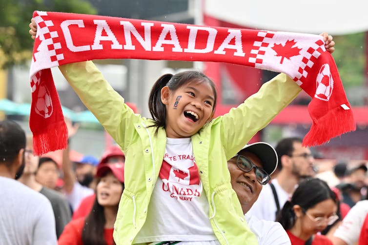 A young girl holds up a scarf that says Canada