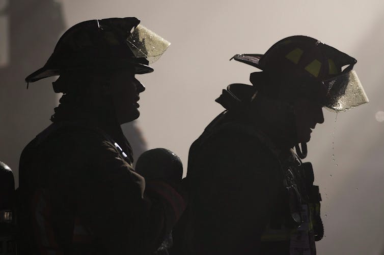 Two firefighters seen silhouetted against a smoky background