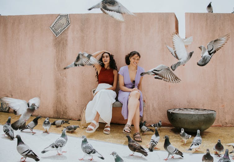 Pigeons surrounding two people sitting on a bench laughing