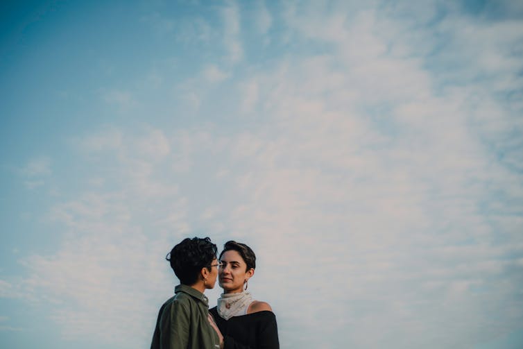 Two women, intimately close, against a large sky.