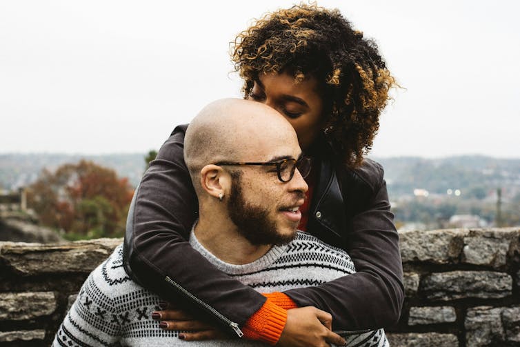 A woman hangs over a man's shoulders affectionately.