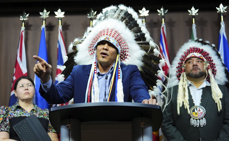 First Nations chiefs in traditional regalia stand at a podium.