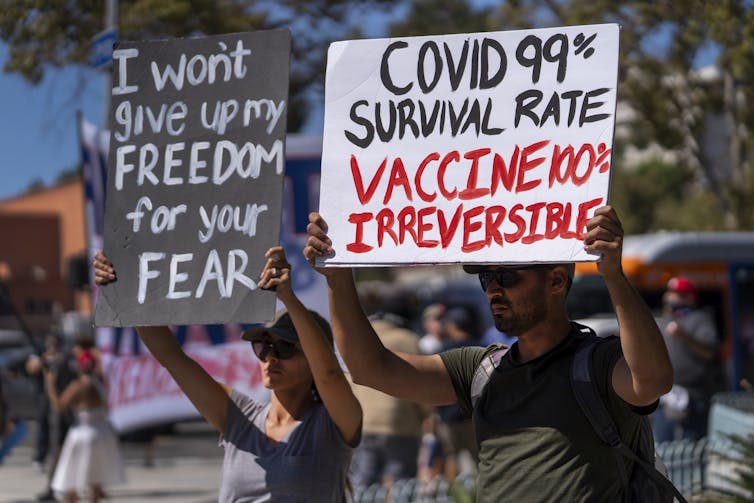 Protesters hold signs that say 'I won't give up my freedom for your fear' and 'COVID 99% survival rate/vaccine 100% permanent'