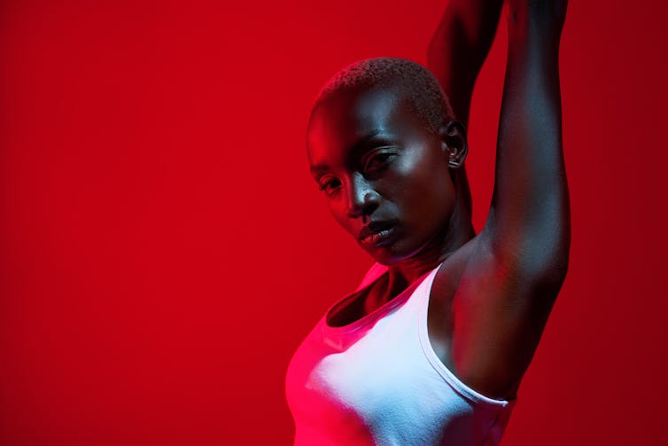 Close up, cropped image of woman in white vest stretching her arms above her head in infrared lighting