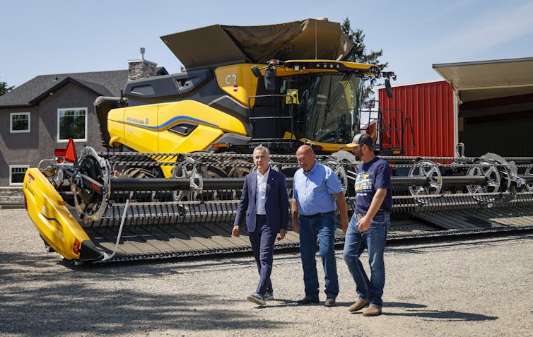 Three white men walk past a combine