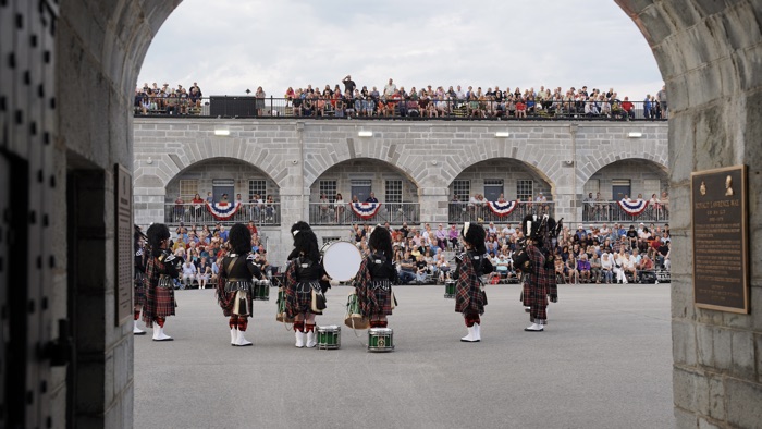 band in kilts playing before spectators on bleachers inside old limestone parade square