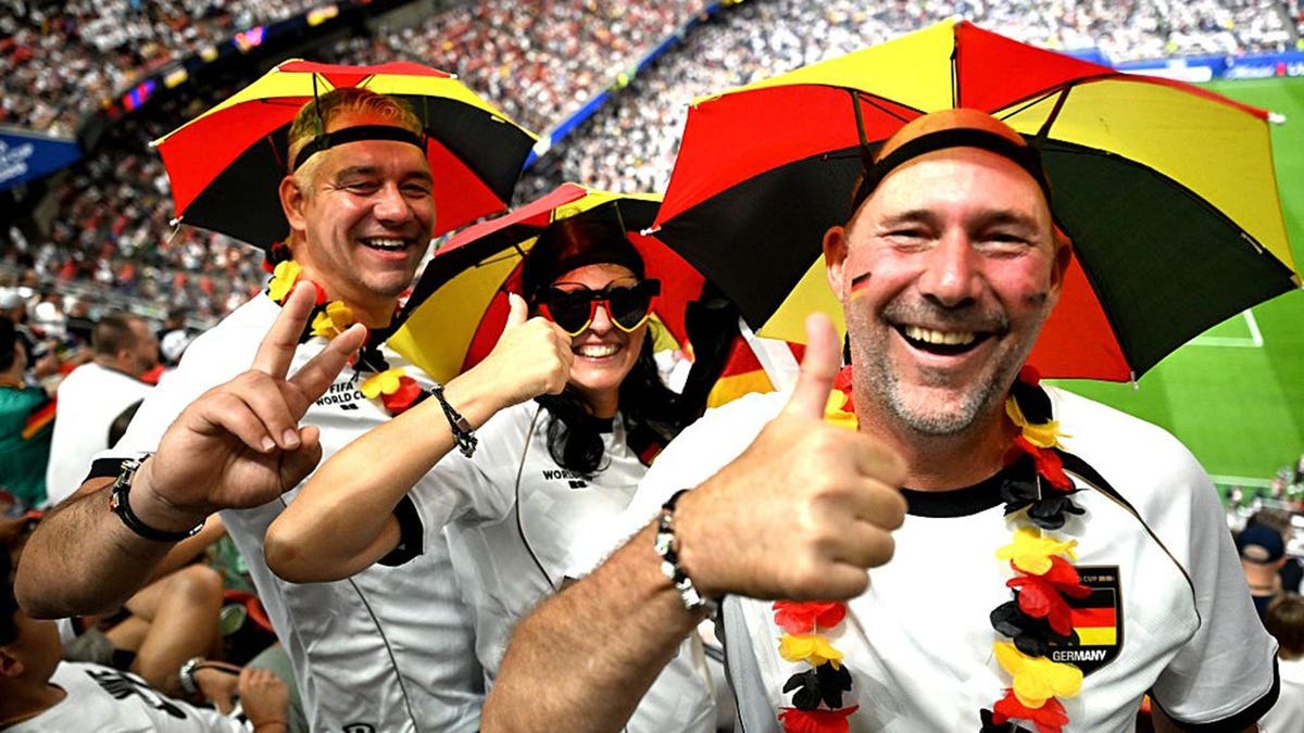 soccer fans in German flag umbrella hats give a thumbs up to the camera