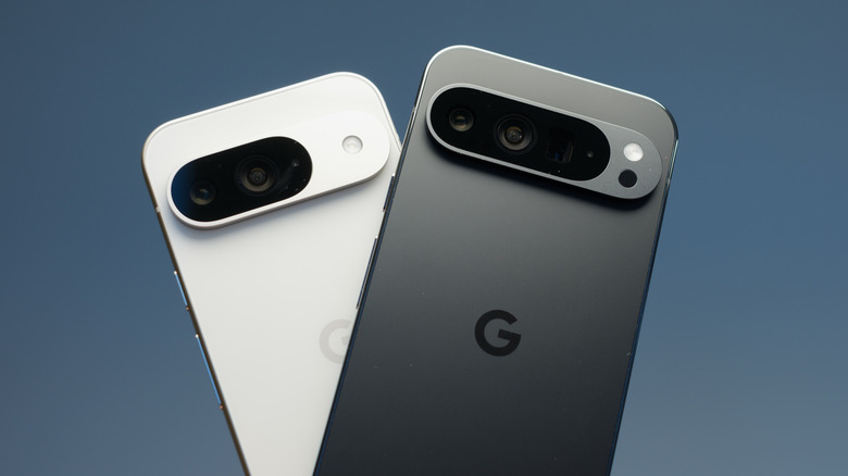 A white Google Pixel phone stands behind a black Google Pixel phone, both devices are against a black/gray backdrop