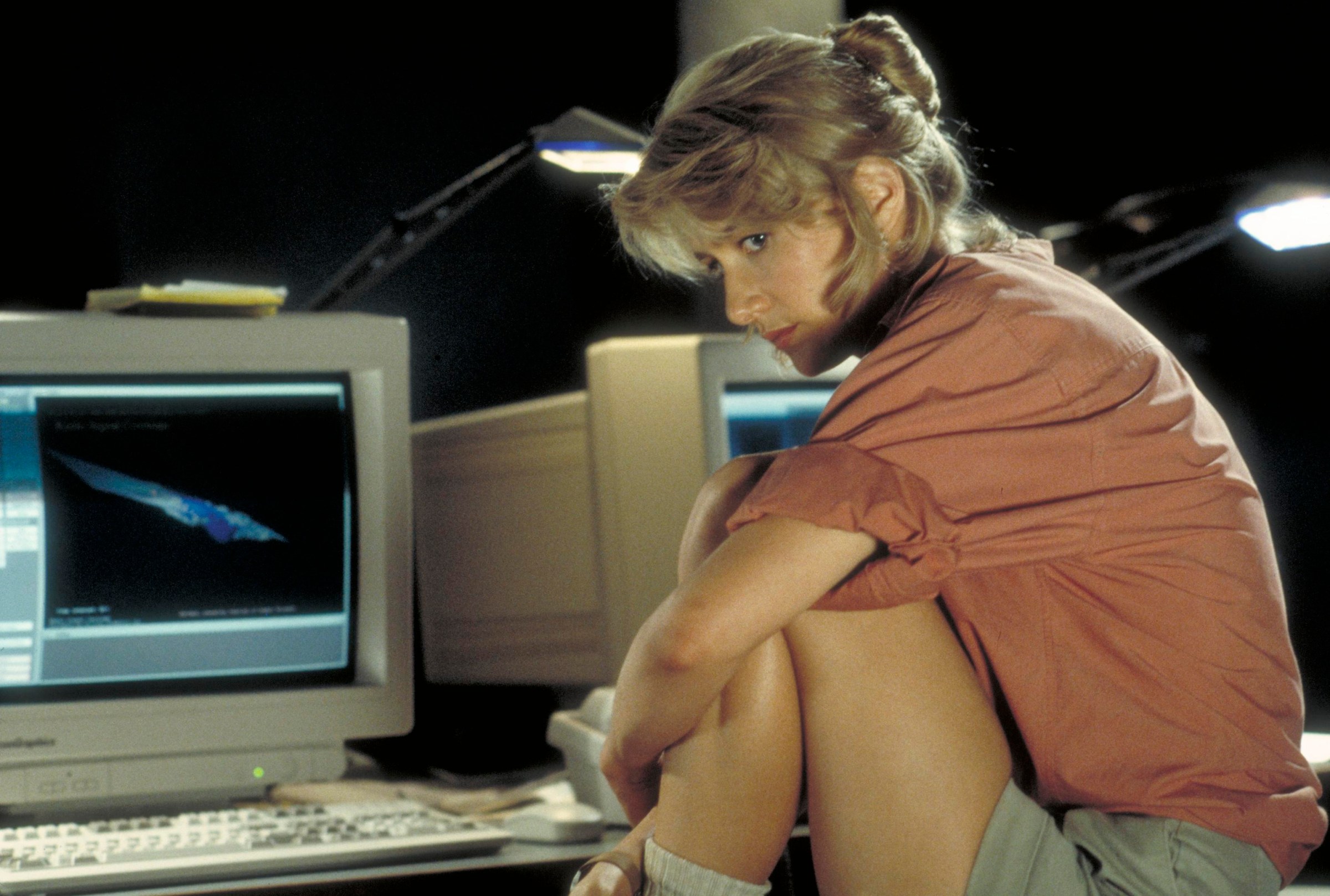 Laura Dern sitting in front of a desk with a computer on the set of Jurassic Park.