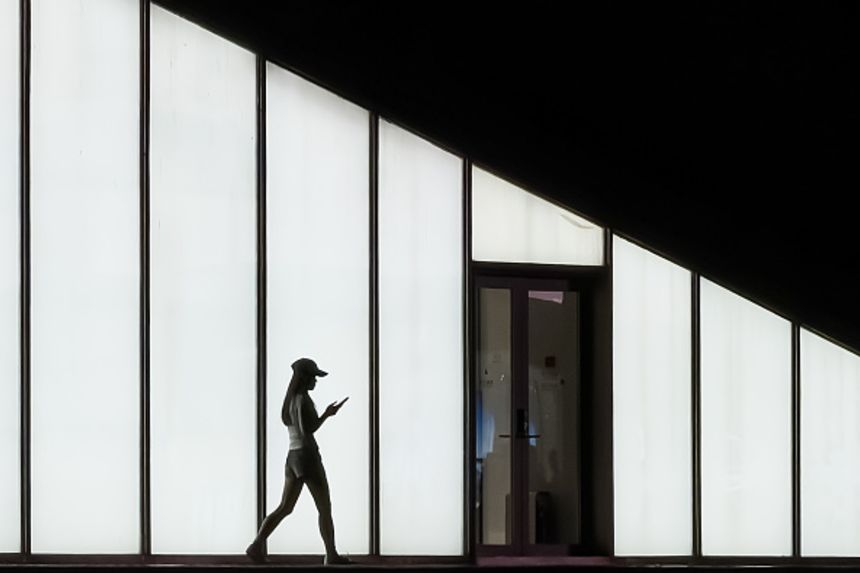 A woman walks while using a smartphone in front of an illuminated wall in Shenzhen, China, on April 27, 2026.