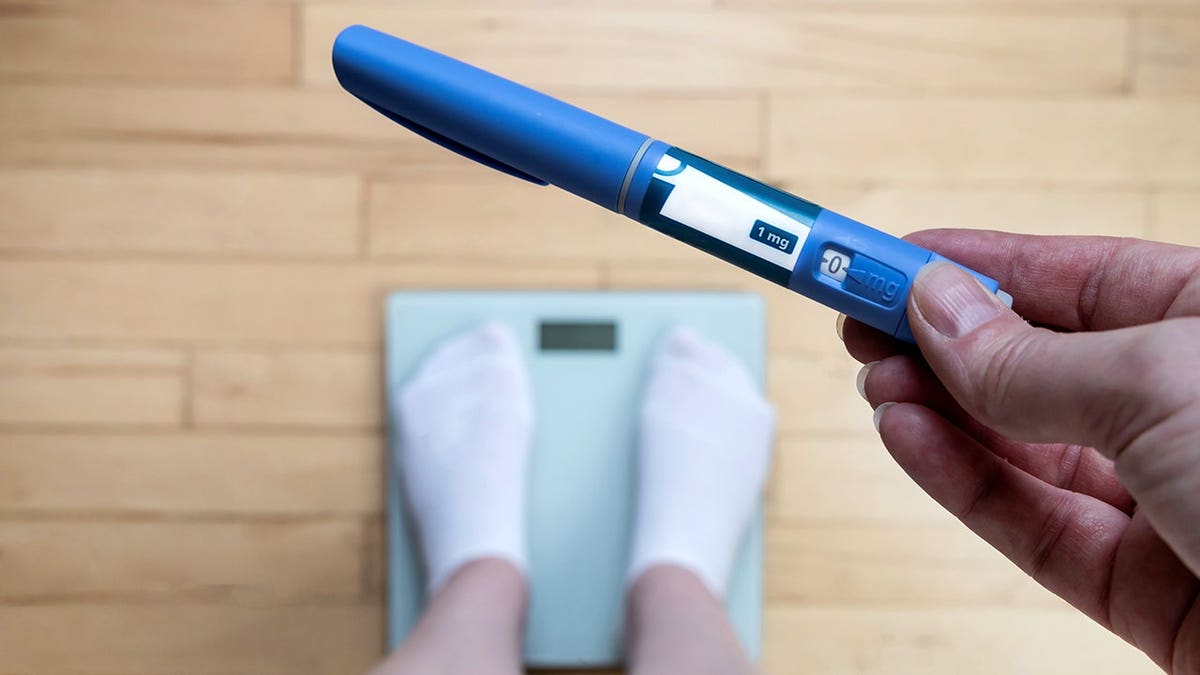 Woman holds Ozempic pen while standing on a scale.