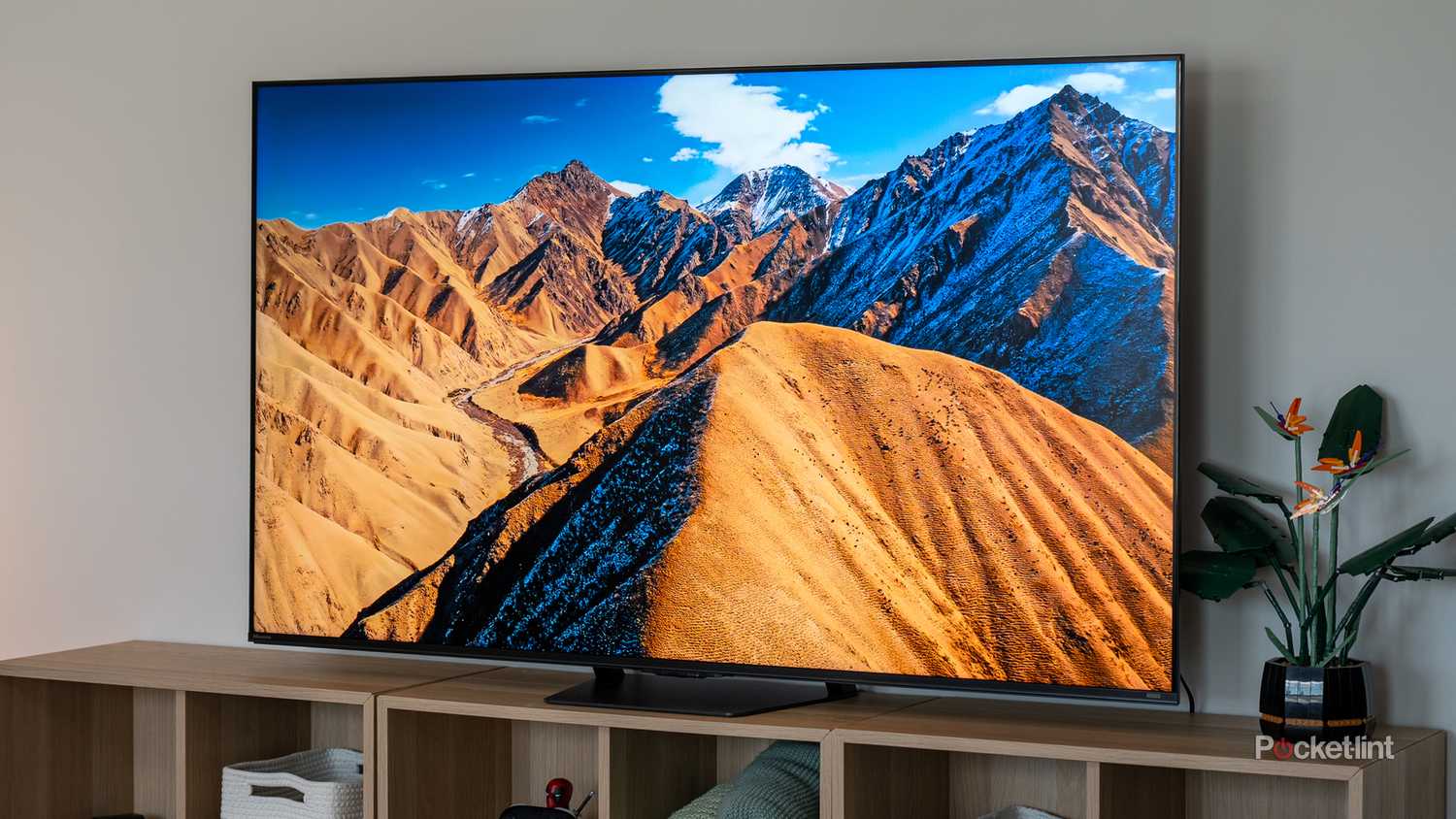 Hisense U7 TV on wood entertainment unit at an angle displaying sun-lit golden arid mountain ridges under a blue sky. (1)