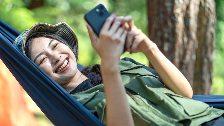 A woman on a hammock smiling while hold her phone