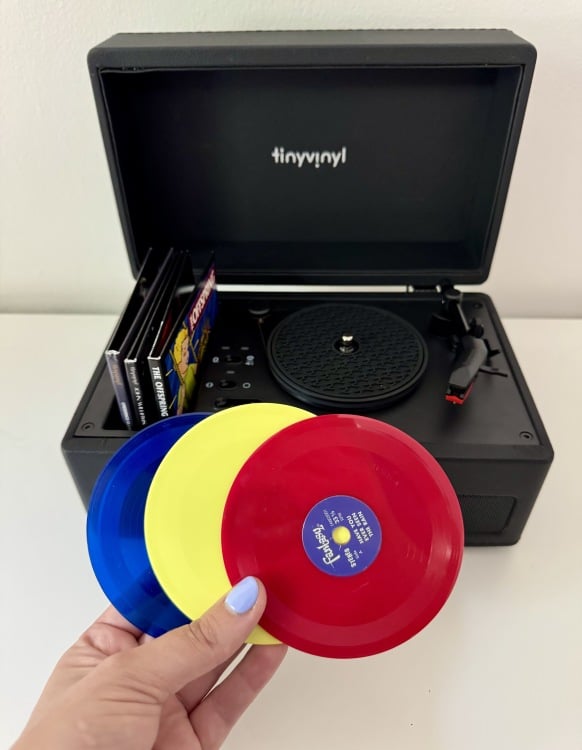 a close-up of a woman's hand holding three tiny vinyl records in front of the tiny vinyl player