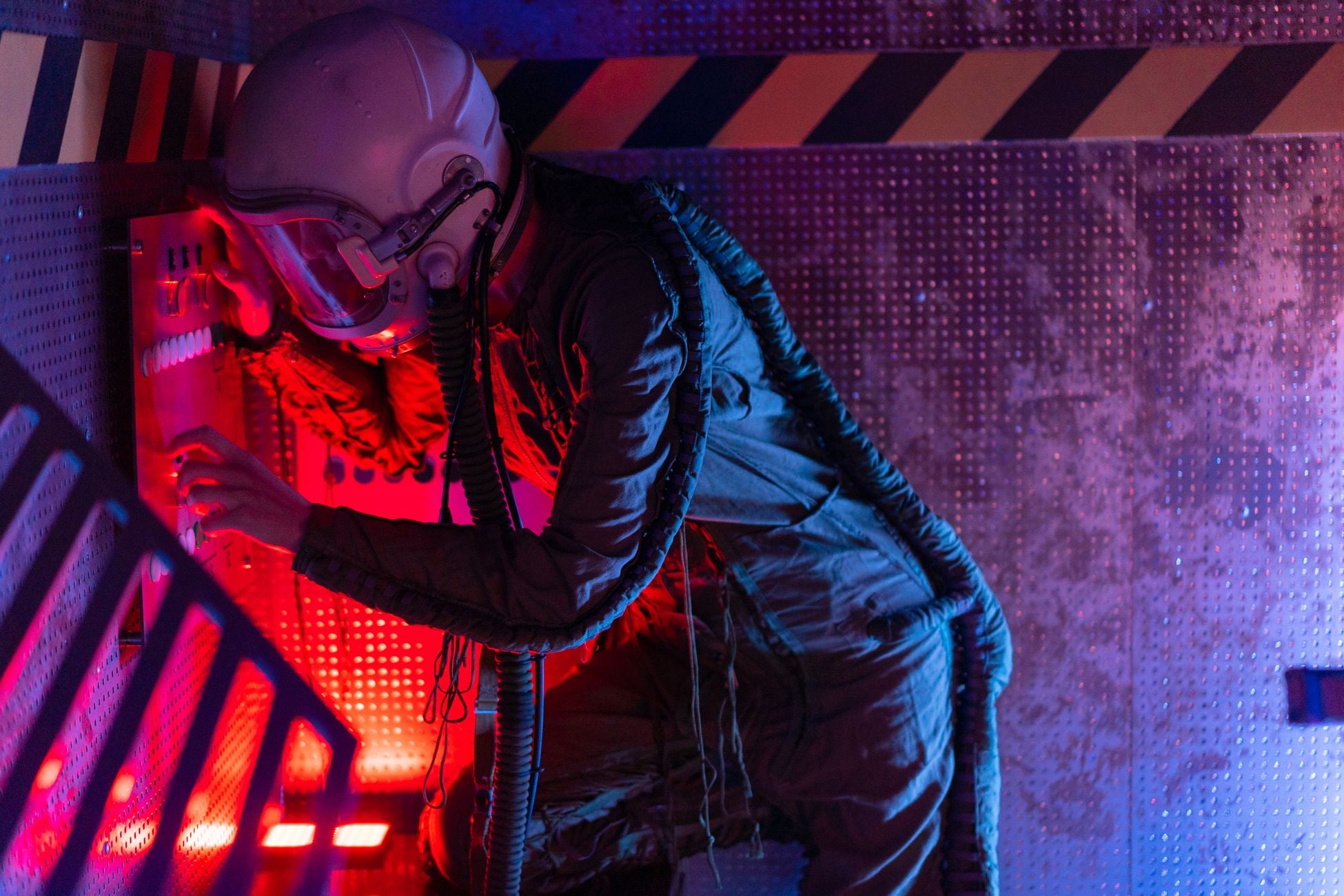 A woman in a spacesuit operates a futuristic control panel, bathed in vibrant red and blue lights.
