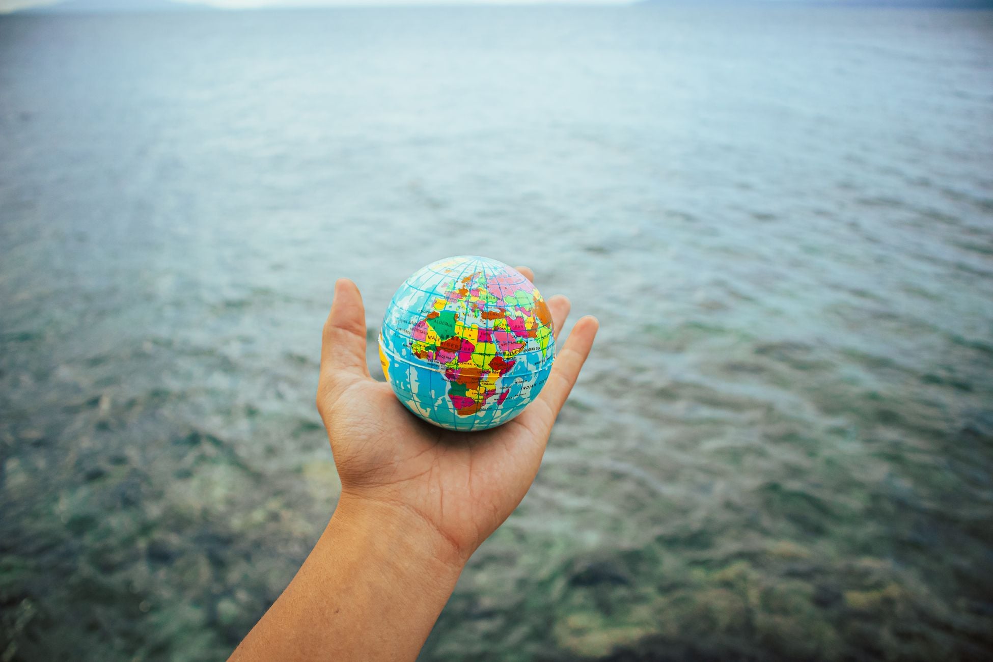 A hand holding a small globe against a vast ocean background, symbolizing global connection.