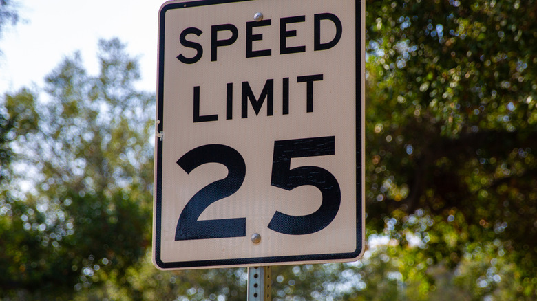 A 25-mph speed limit sign with trees in the background.