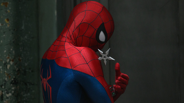 Tom Holland as Peter Parker wearing his superhero suit and grabbing a shuriken stuck in his shoulder in Spider-Man: Brand New Day