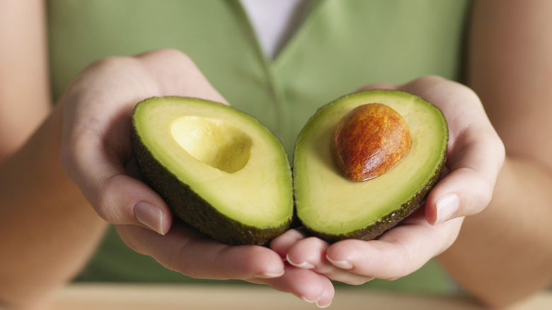 Woman's hands holding two avocado halves