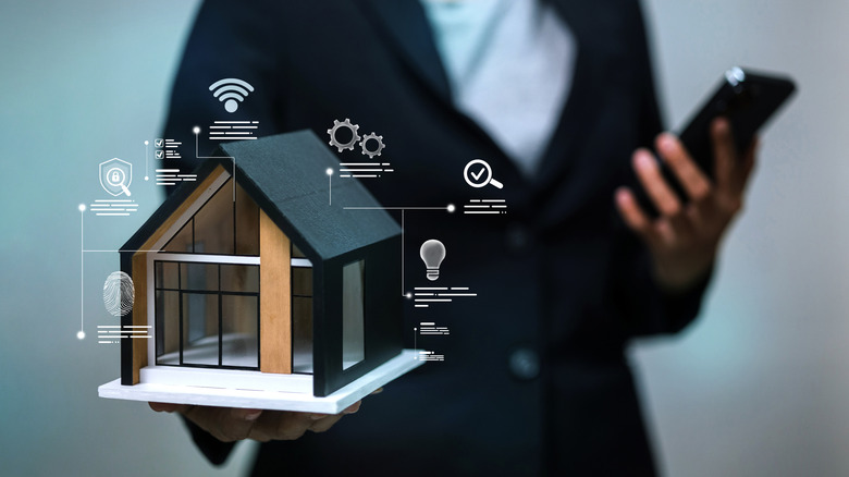 A person holding a phone and a house model, visually depicted as a smart home with icons floating around it
