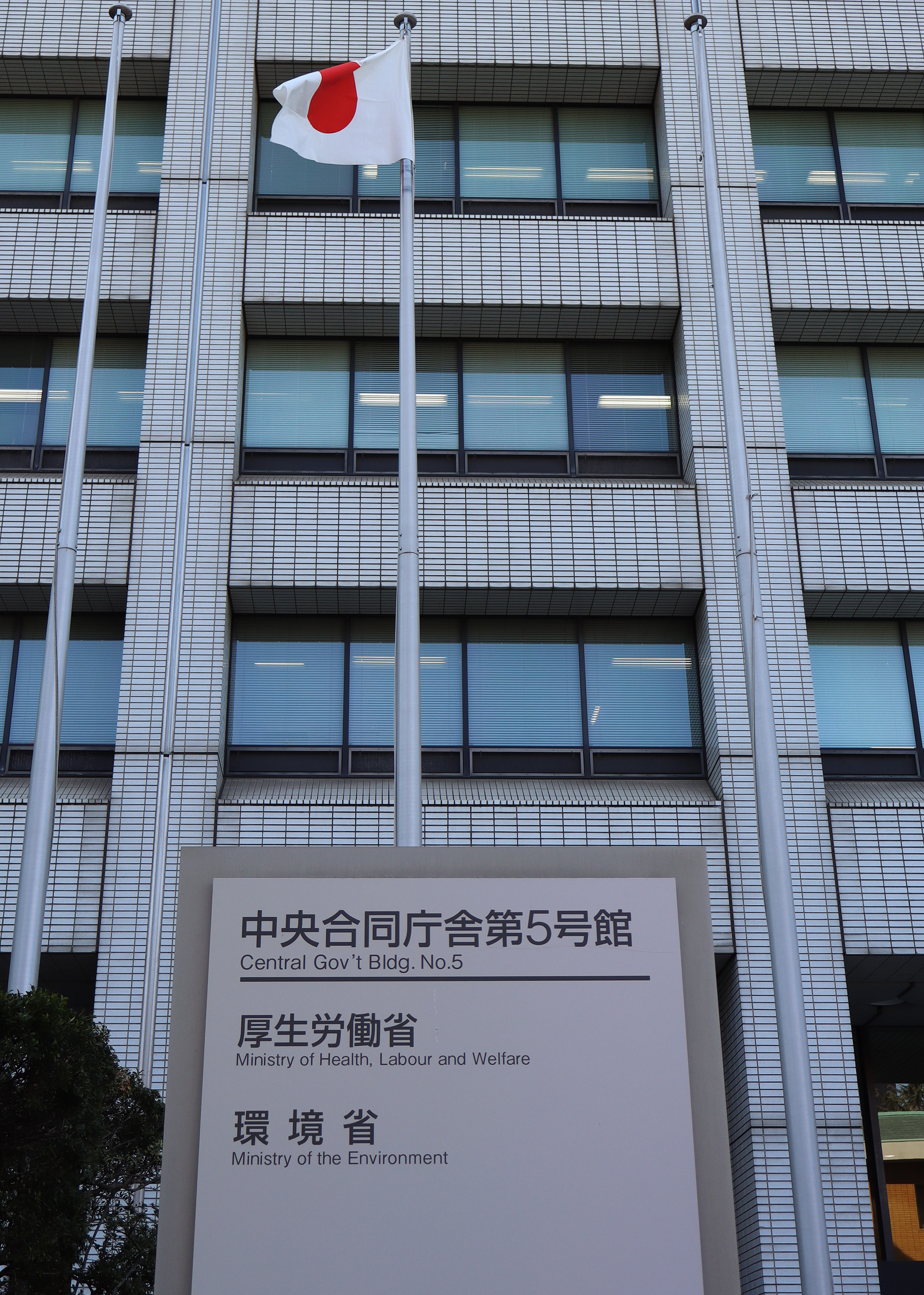 A building with a Japanese flag flying in front of it and a plaque with both English and Japanese writing on it