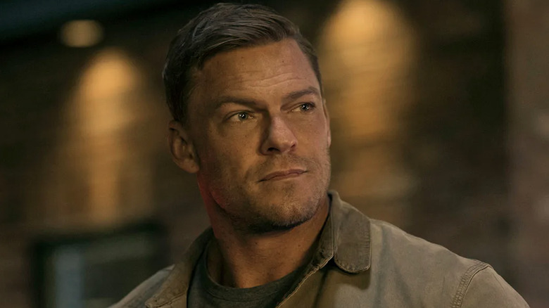Alan Ritchson as Jack Reacher wearing a brown work jacket.