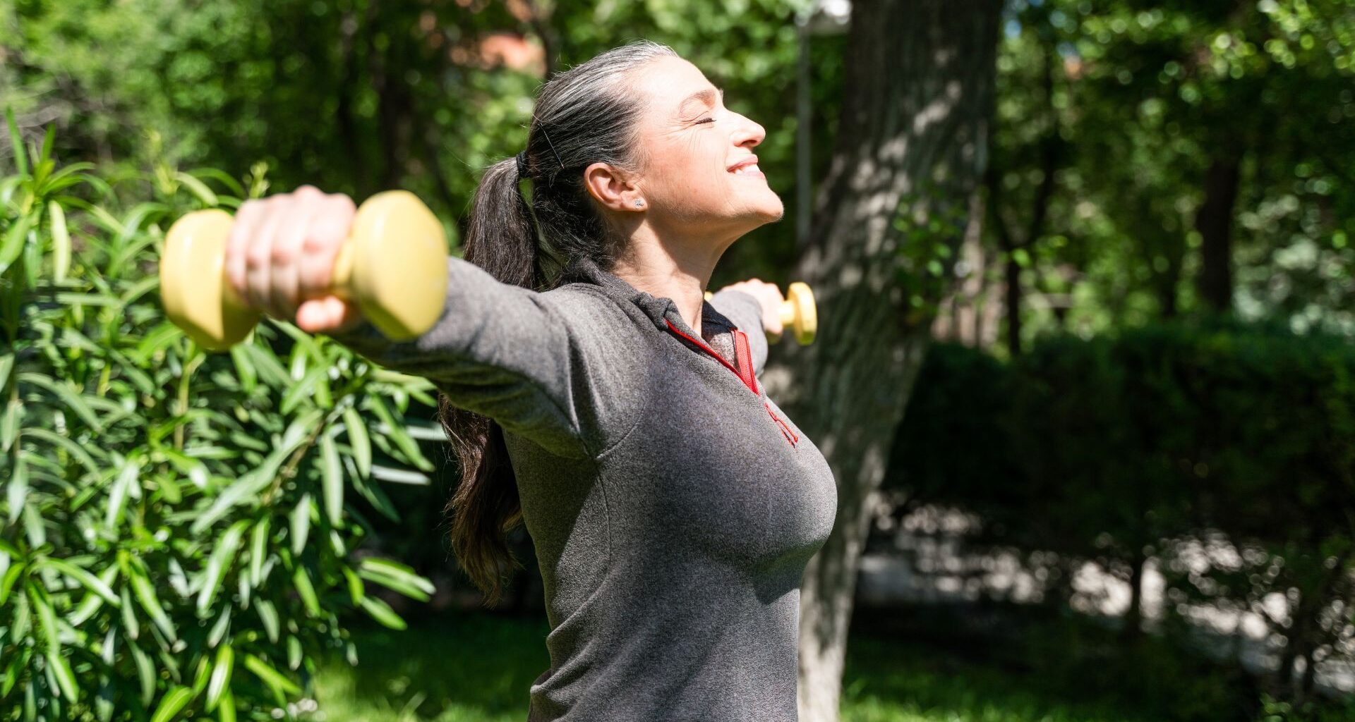 Woman doing lateral raise exercise in garden sunshine
