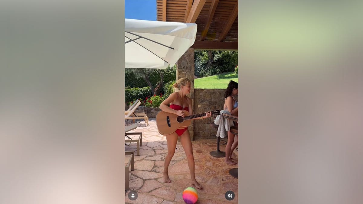 Kate Hudson holding a guitar while in a red bikini.