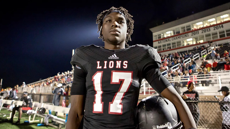 A football player stands holding his helmet by the stands in Last Chance U