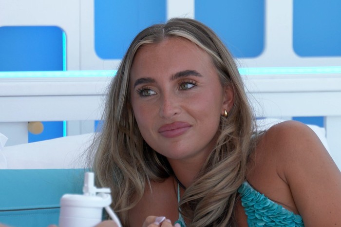 Love Island S13 A woman wearing a light blue bikini lying down on a day bed smiling as she looks up at someone.
