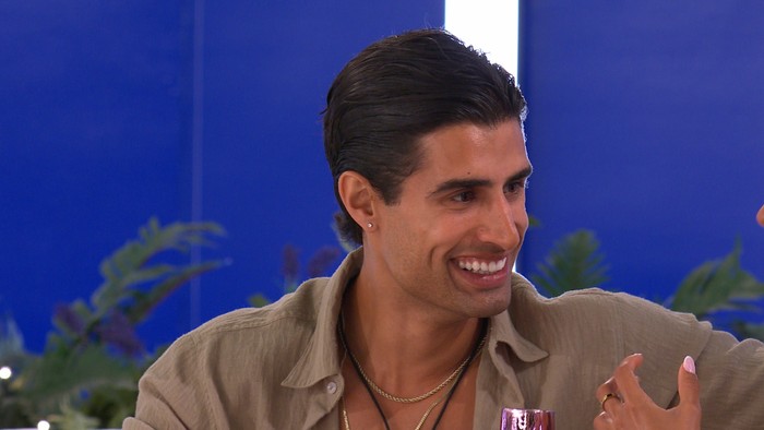 Love Island S13 Samraj wearing a light brown shirt, smiling ahead as he looks over at someone.