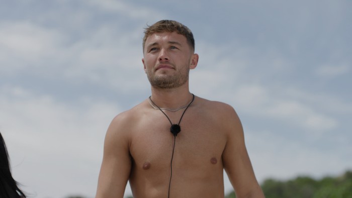Love Island S13 A topless man walking ahead with a microphone around his neck.
