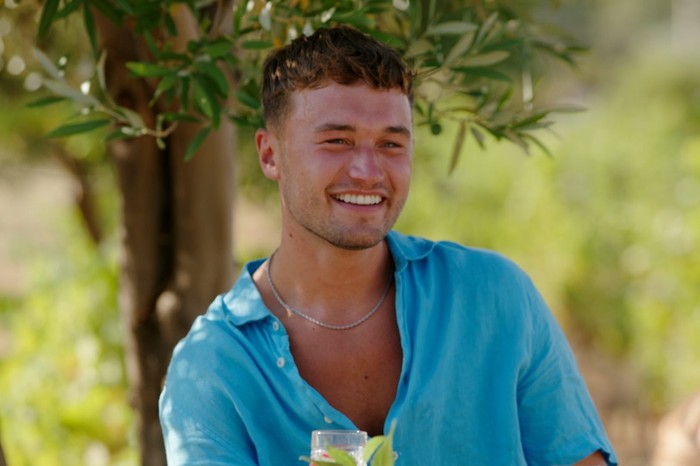 Love Island S13 Finley sat back wearing a light blue shirt, smiling ahead.