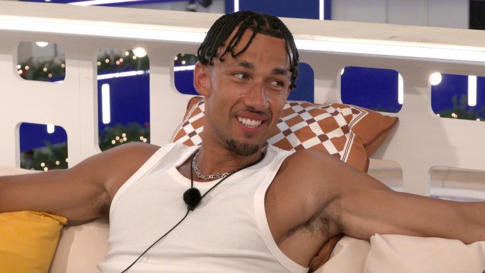 Love Island S13 Jordon sat lying down on the terrace, smiling as he looks over at someone.