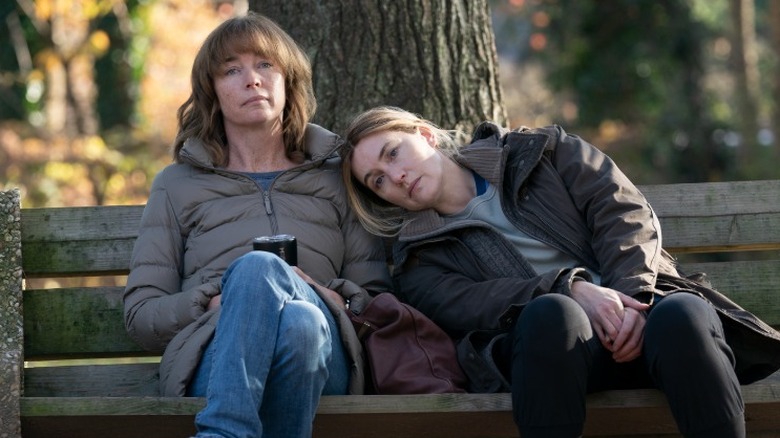 Mare Sheehan sitting on a park bench leaning her head on Lori's shoulder in Mare of Easttown