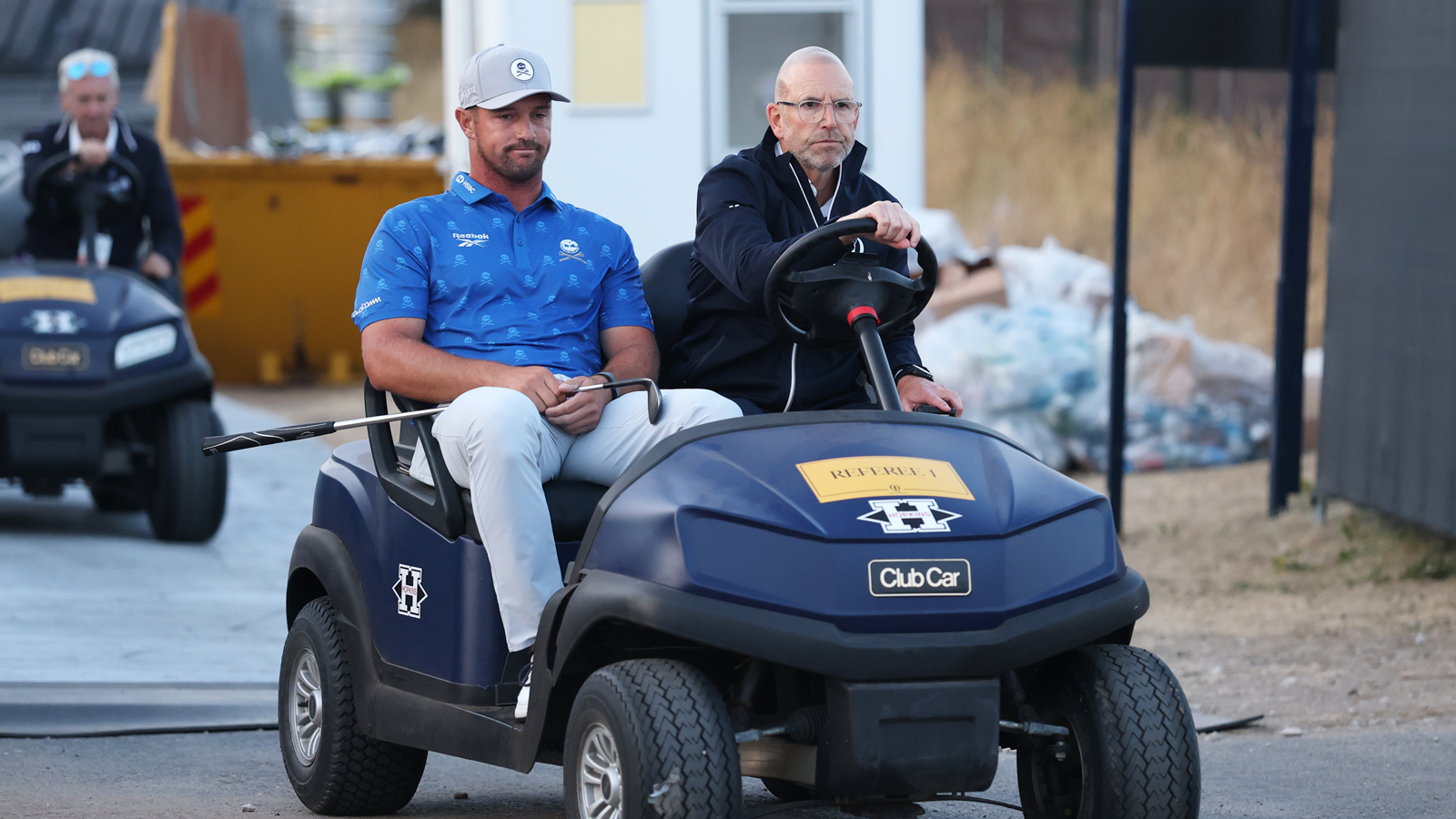 Bryson DeChambeau and a rules official drive in a golf cart