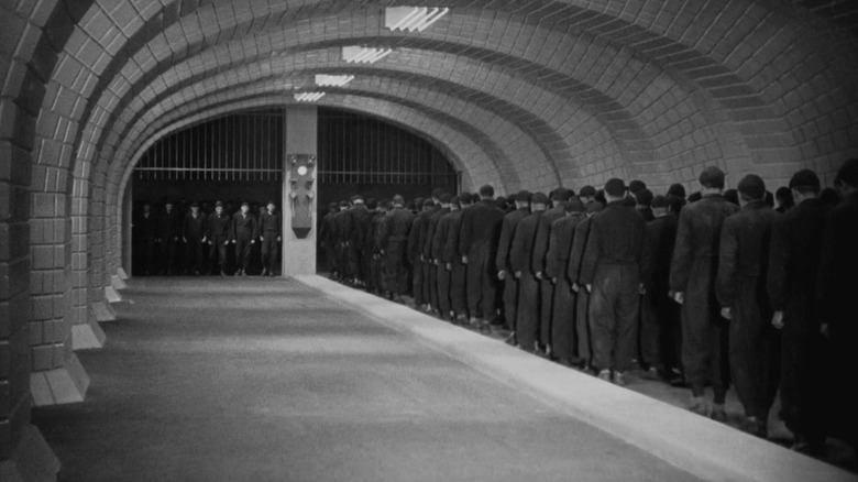 A shot of the persecuted workers that power the city in Metropolis, all gathered together and walking in a congregation through the oppressive walls and gates within the city.