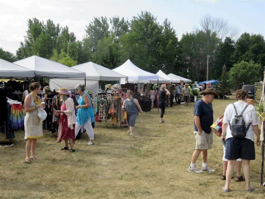 people browsing racks of clothes and other items under white tent shelters on a lawn.