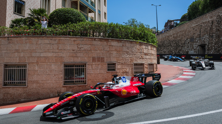 Formula 1 cars rounding a tight downhill curve toward the camera between stone walls on the track at the Mondaco Grand Prix