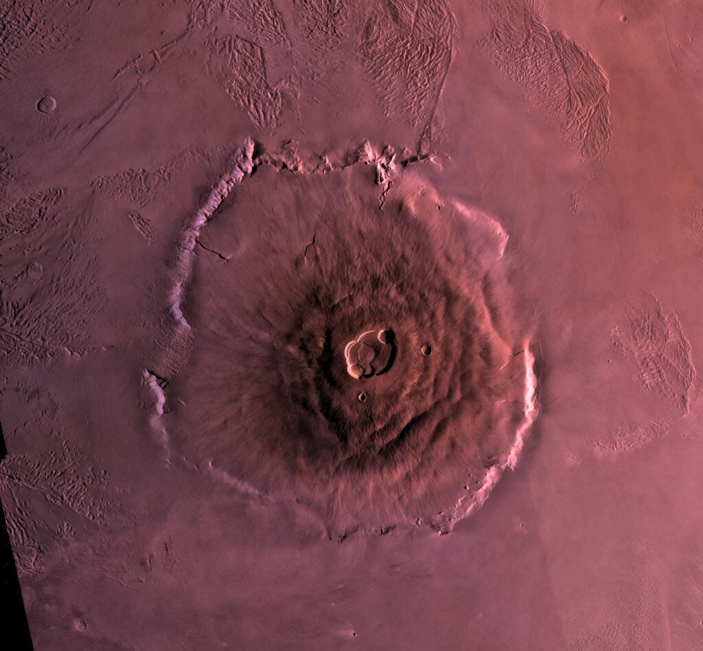 Olympus Mons stands nearly three times the height of Everest, yet standing at its base you would not see a mountain at all, because its slopes rise so gently across roughly 600 kilometres that the summit sits well beyond the Martian horizon and the ground at your feet looks almost flat
