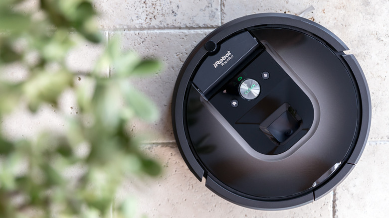 A roomba on a ceramic floor, next to a blurry house plant