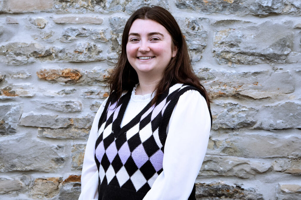 A woman poses for the camera in front of a stone wall.