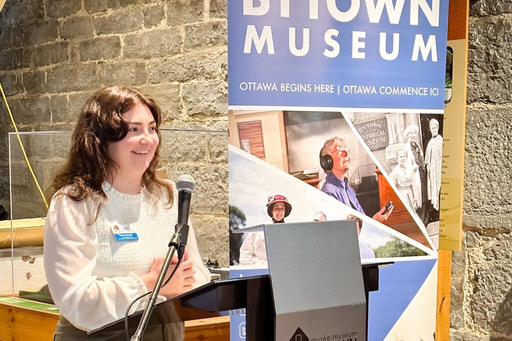 A woman delivers a speech at a podium inside the Bytown Museum.