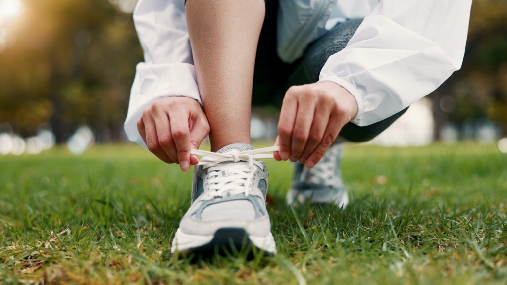 A person in athletic wear tying their running shoe laces on a grassy field.