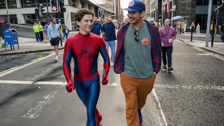 Tom Holland as Peter Parker in his superhero suit walking next to director Destin Daniel Cretton in front of several crew members on the set of Spider-Man: Brand New Day