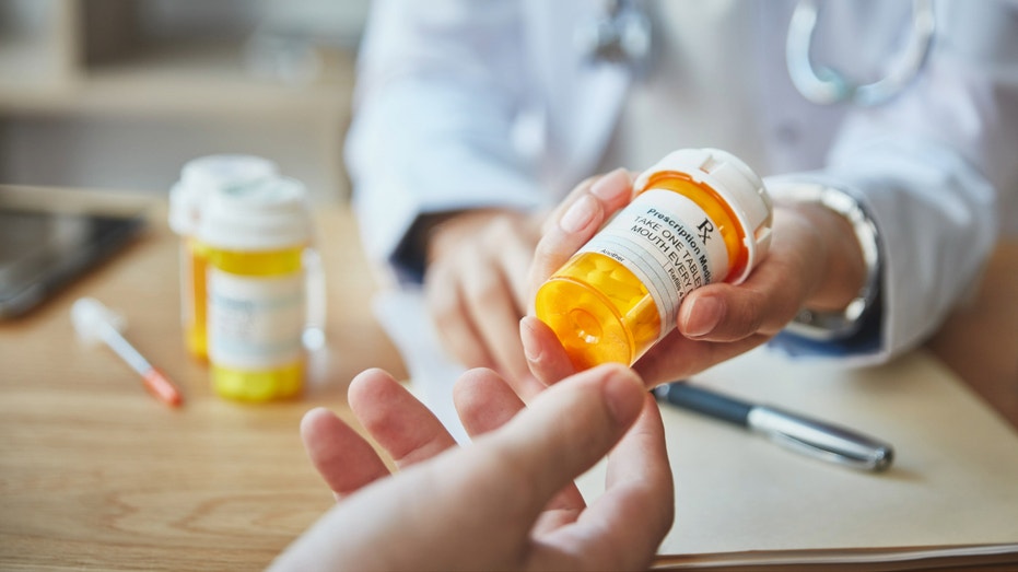 A pharmacist hands a patient a bottle of prescription medication.
