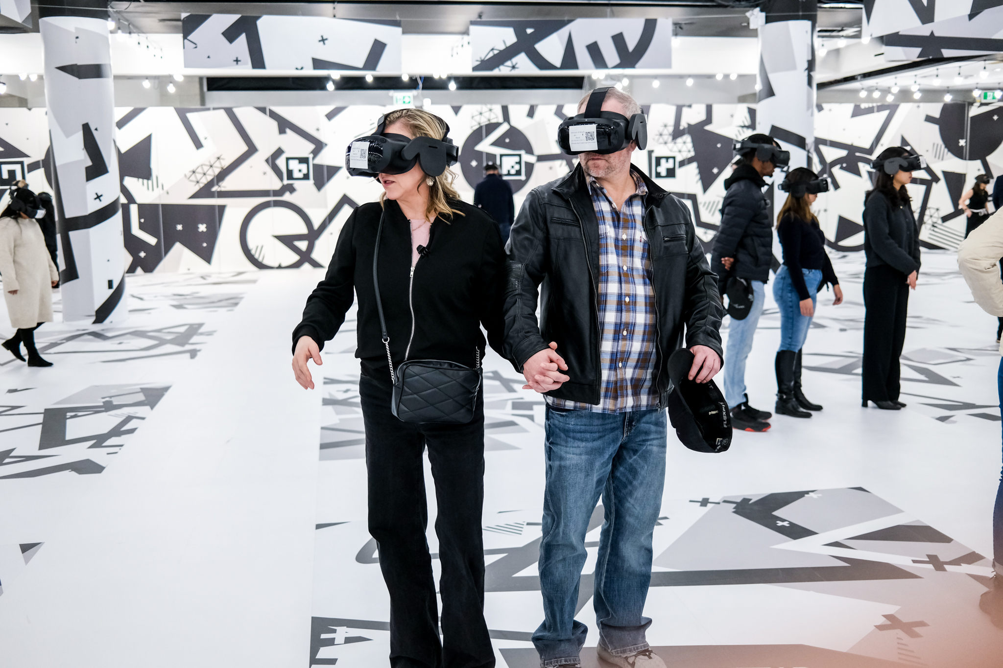 Two people with VR glasses in a white room holding hands.