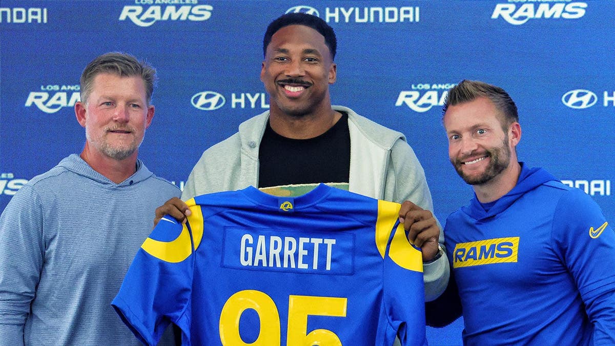 Myles Garrett #95 of the Los Angeles Rams poses with general manager Les Snead and head coach Sean McVay during a press conference