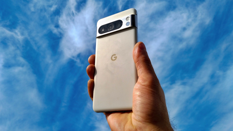 A silver Google Pixel 8 being held up to a semi-cloudy sky in a user's right hand